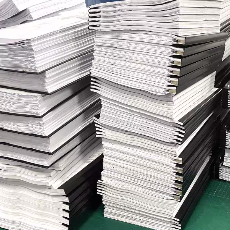 Wysokie stosy profesjonalnie oprawionych projektów budowlanych w czarnych okładkach na stole montażowym w technikadruku.pl – realizacja dużego zamówienia dokumentacji technicznej